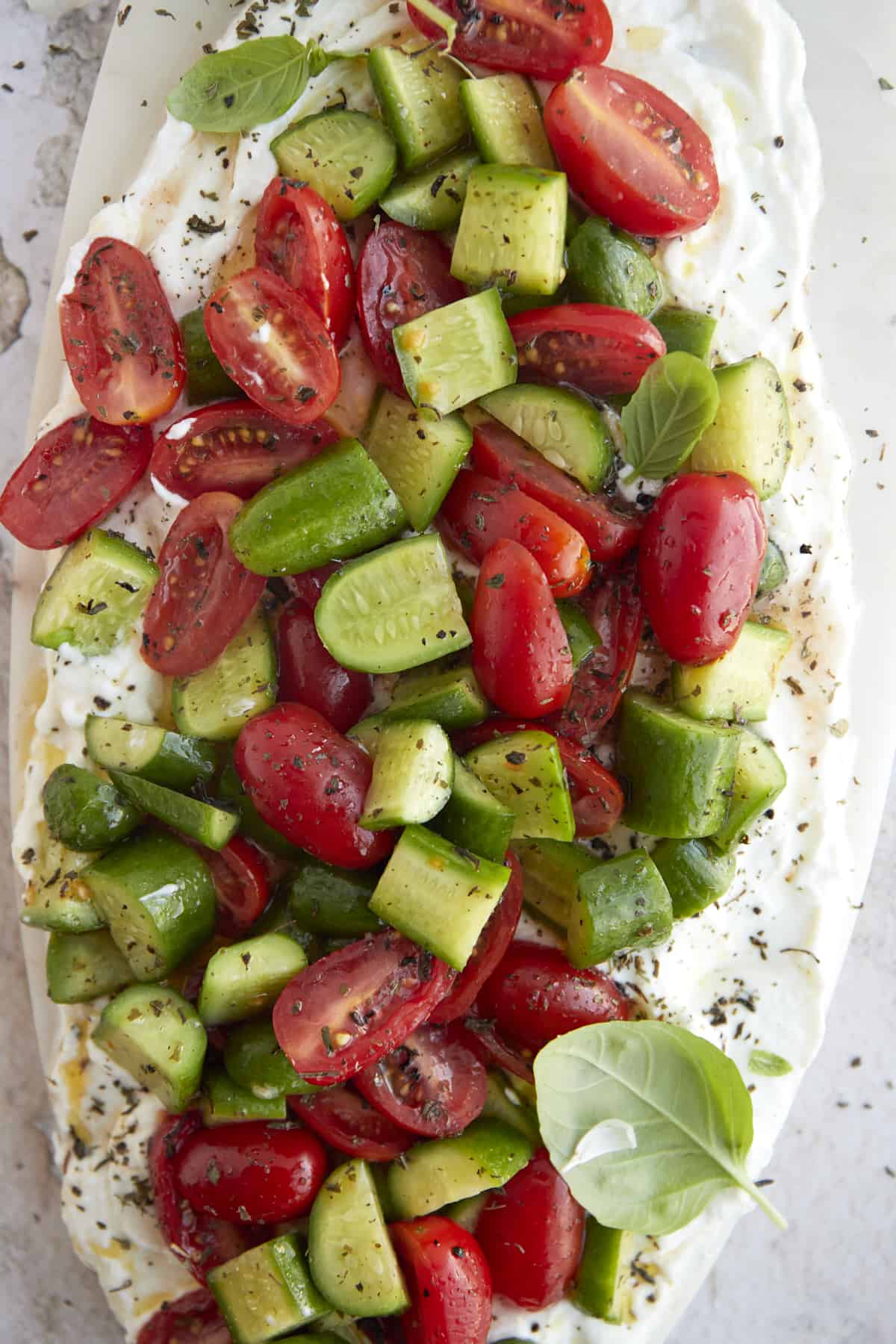 overhead image of a cucumber and tomato salad layered over whipped feta topped with fresh herbs and seasonings