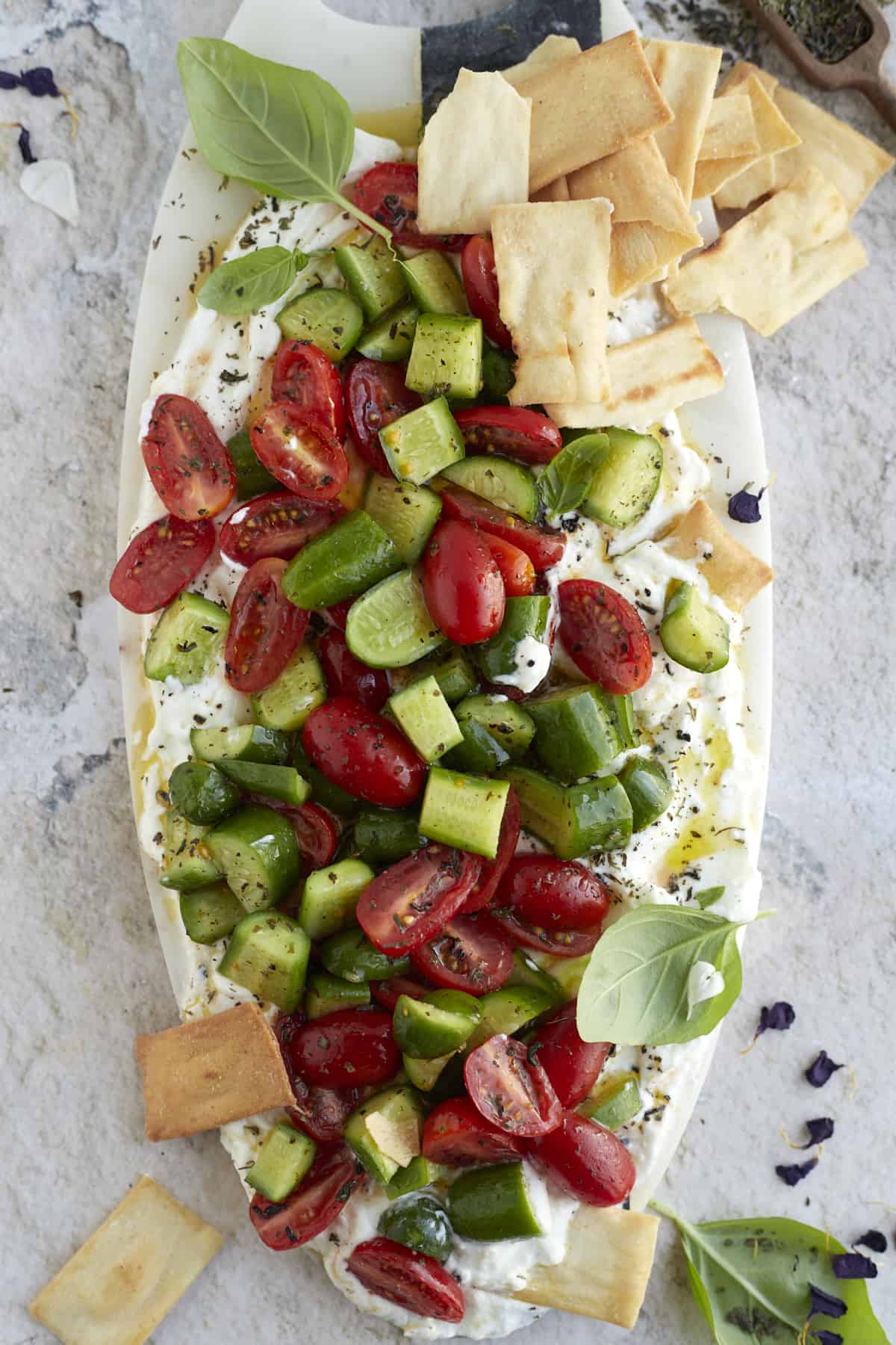 whipped feta with tomato and cucumber salad on a serving board with pita chips on the side