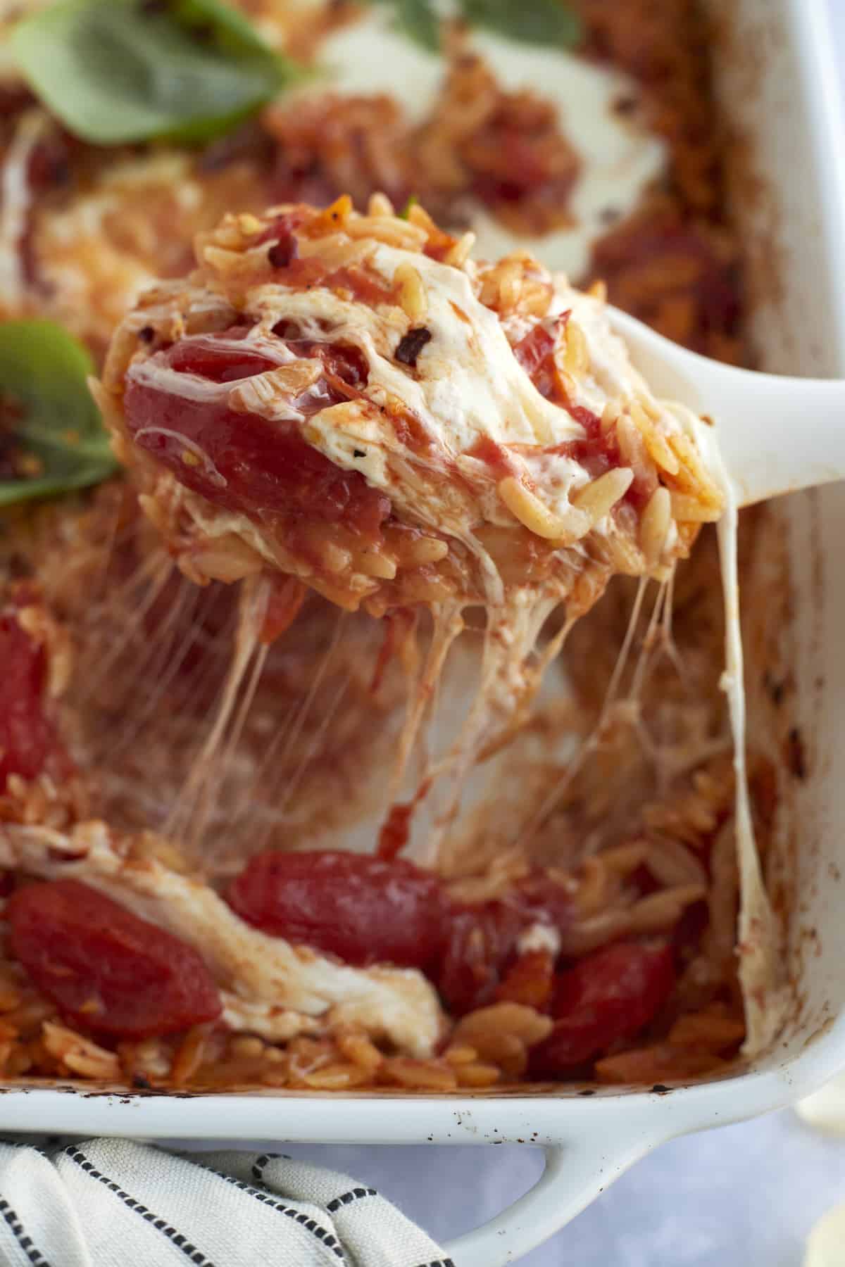a serving of caprese baked orzo pasta being lifted from a casserole dish