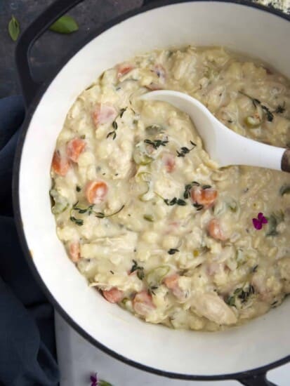 a bowl of creamy chicken noodle soup being scooped up with a spoon.