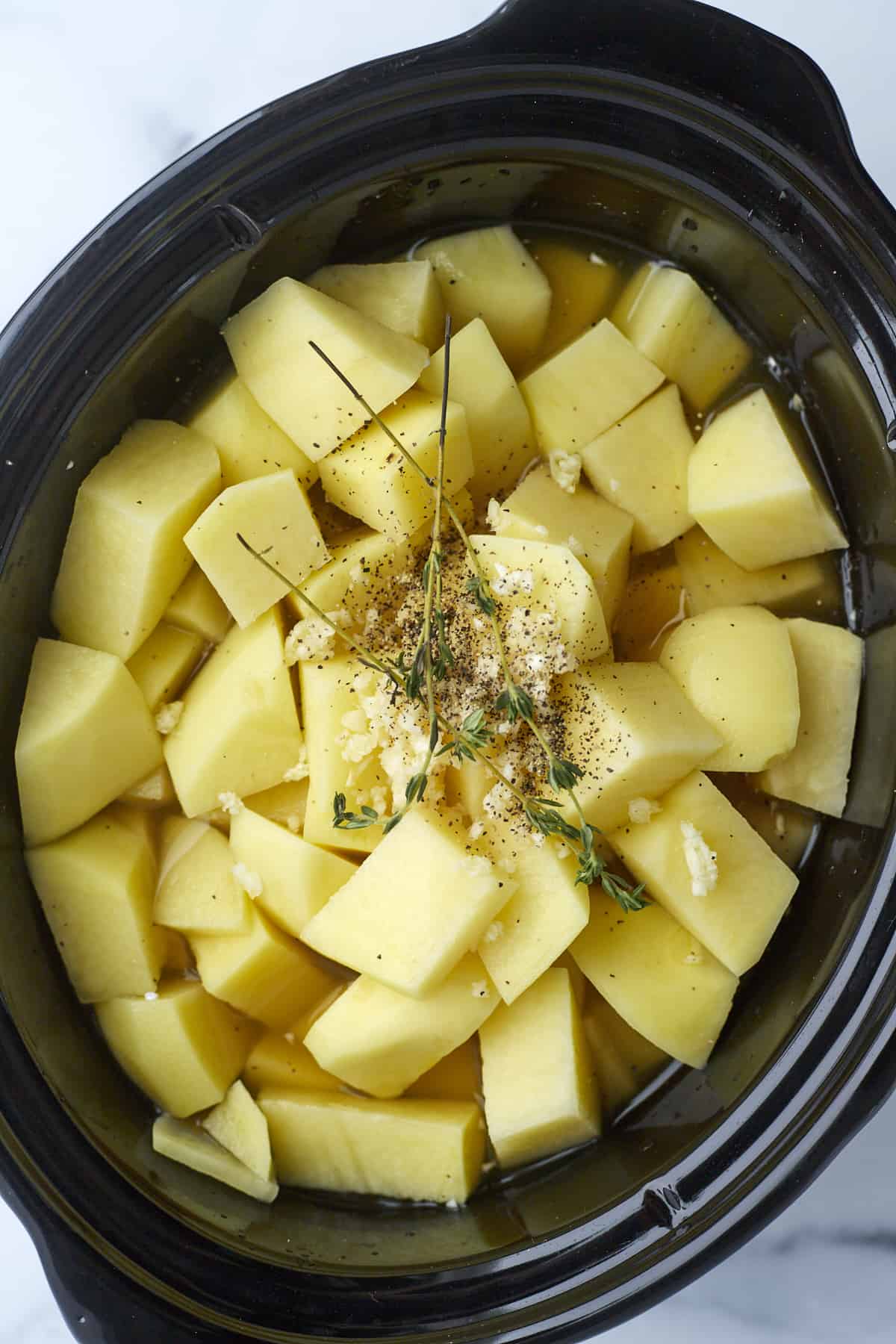 cubed potatoes in a slow cooker with vegetable broth, garlic, and herbs.