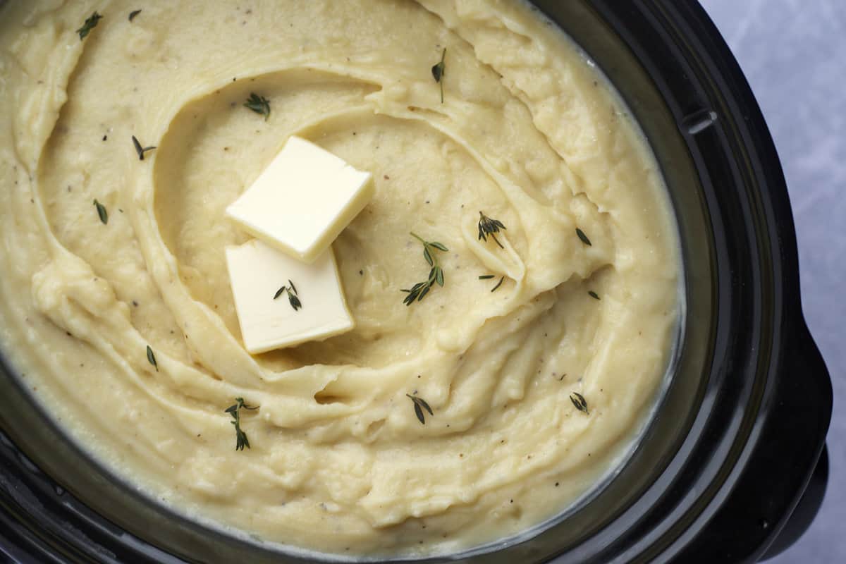 creamy mashed potatoes in a slow cooker topped with two pads of butter