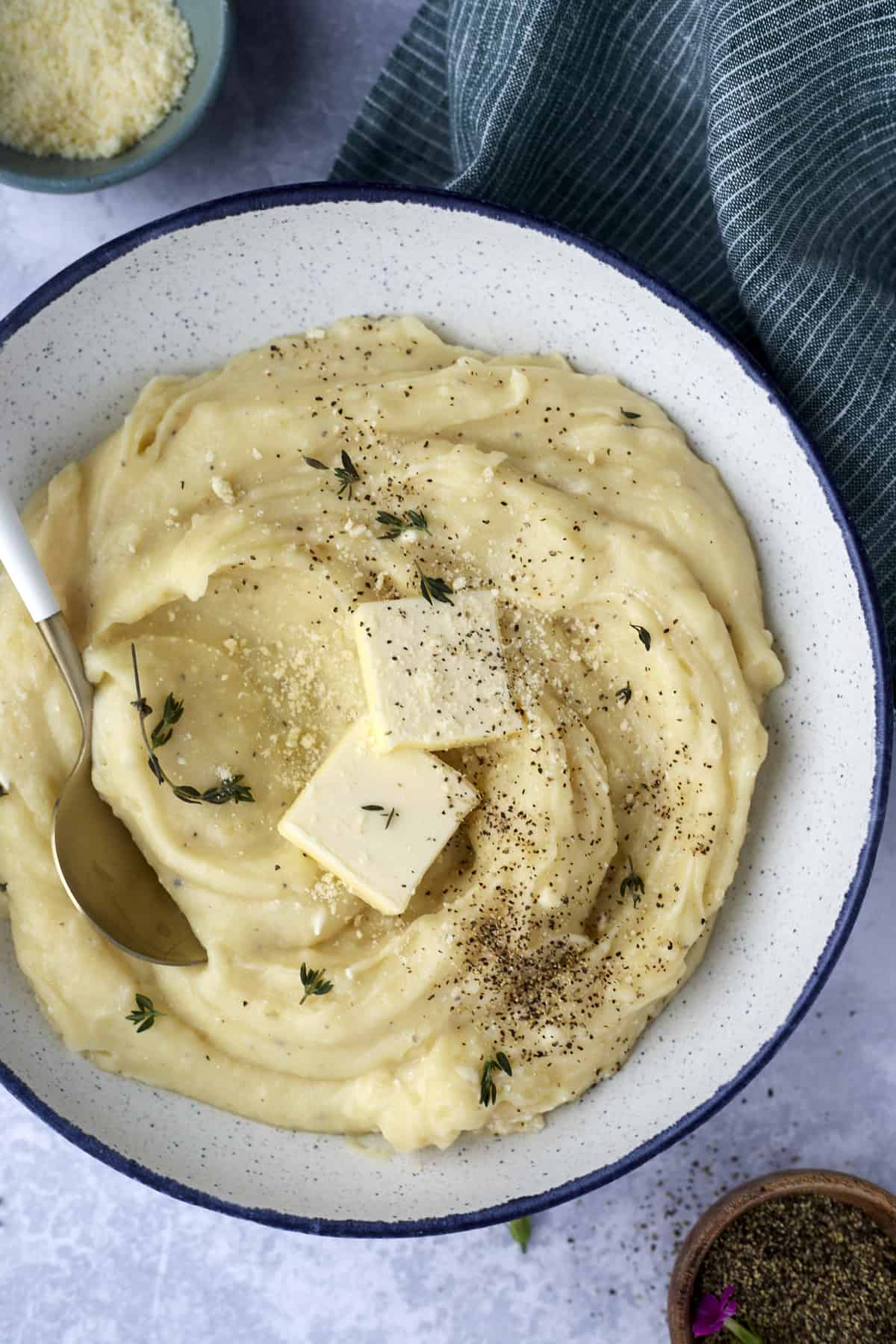 creamy slow cooker mashed potatoes in a bowl topped with two pads of butter, garlic, and pepper