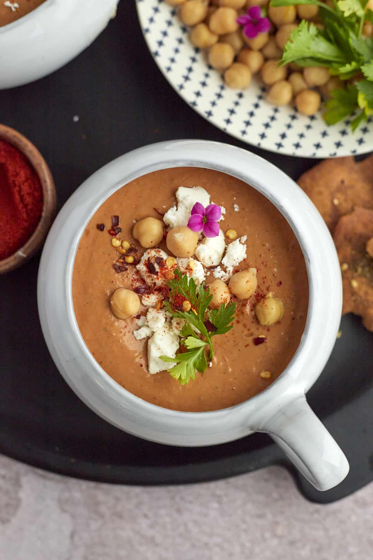 a bowl of Moroccan Spicy Tomato Soup topped with feta cheese, chickpeas, fresh parsley, and red pepper flakes