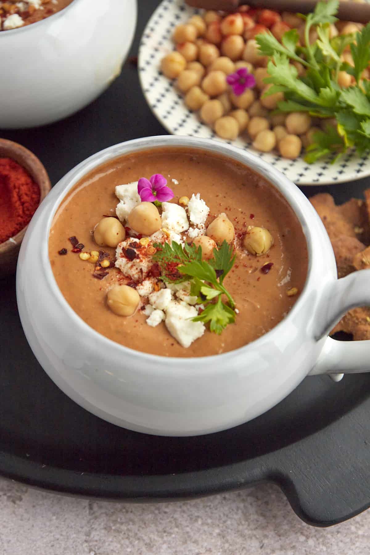 a bowl of Moroccan Spicy Tomato Soup with a plate of chickpeas and fresh parsley in the background for garnishing