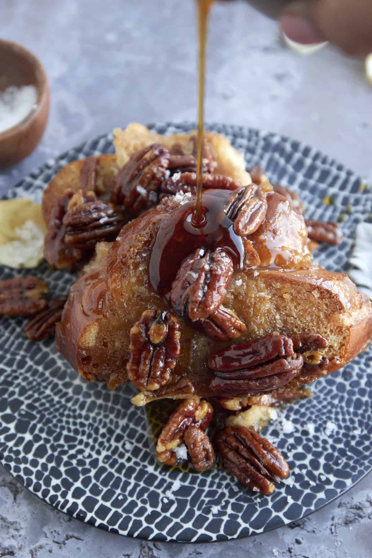 a serving of pecan pie french toast on a plate with maple syrup being drizzled on top 