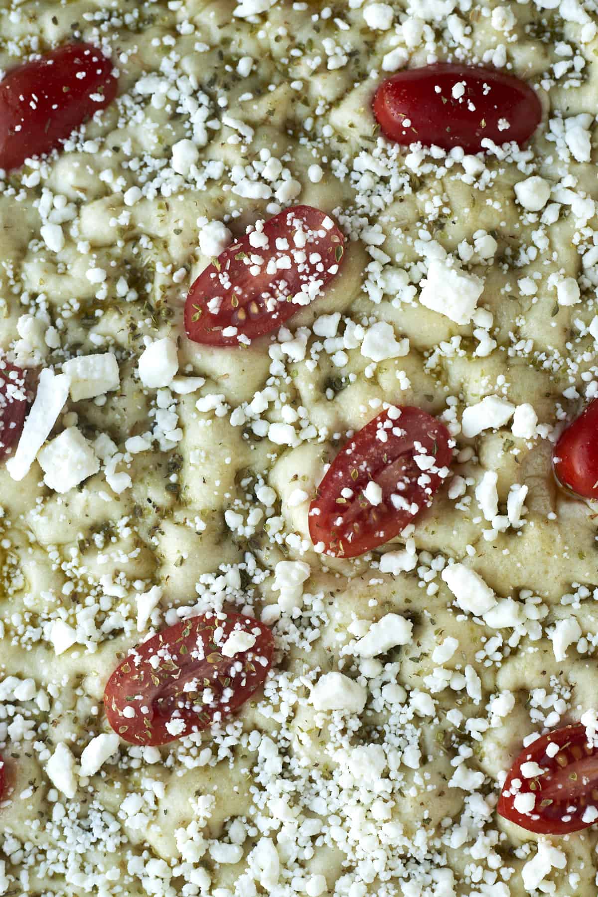 raw easy focaccia bread topped with sliced cherry tomatoes and feta cheese