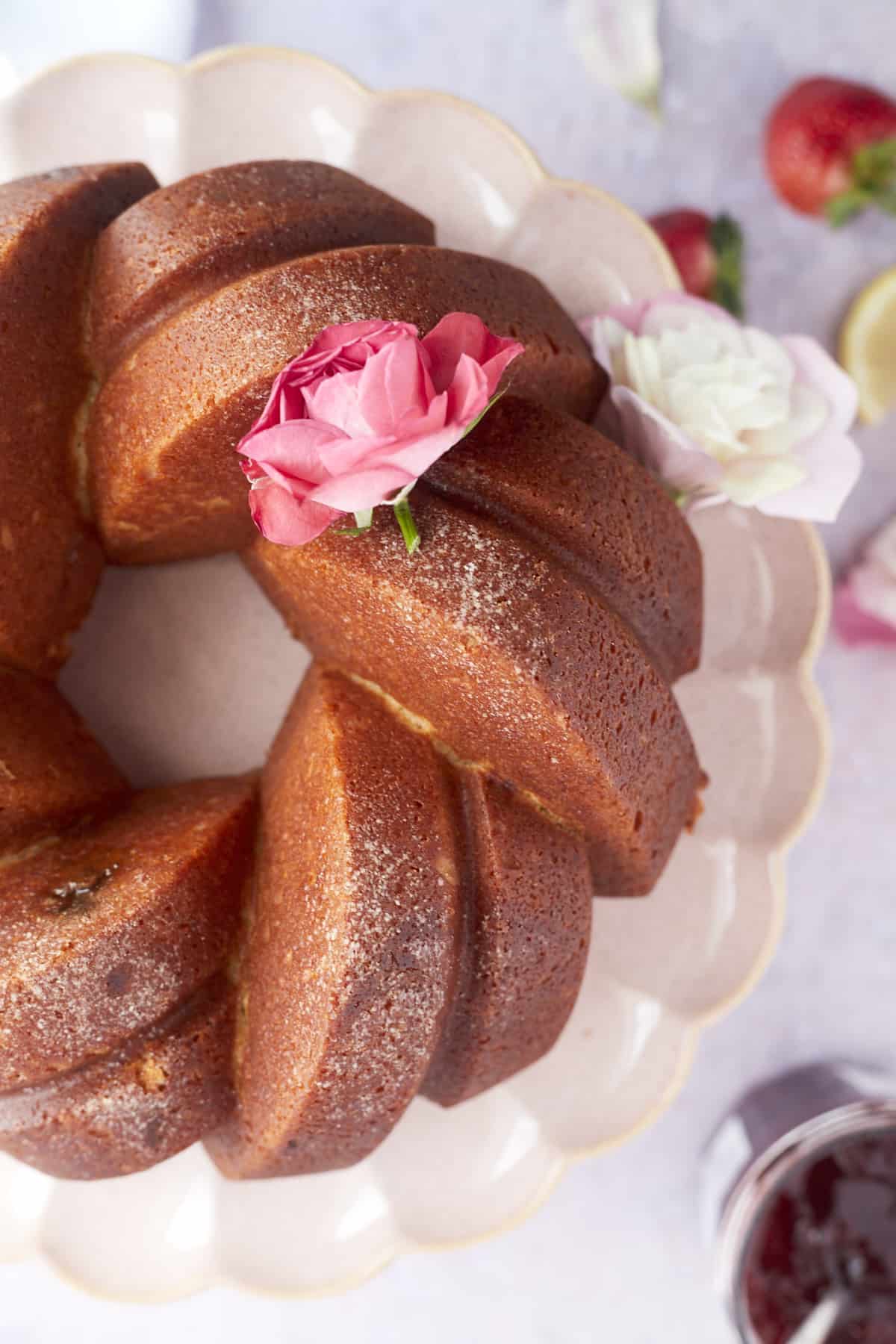 overhead image of a plain baked strawberry lemon bundt cake on a cake stand topped with a pink rose