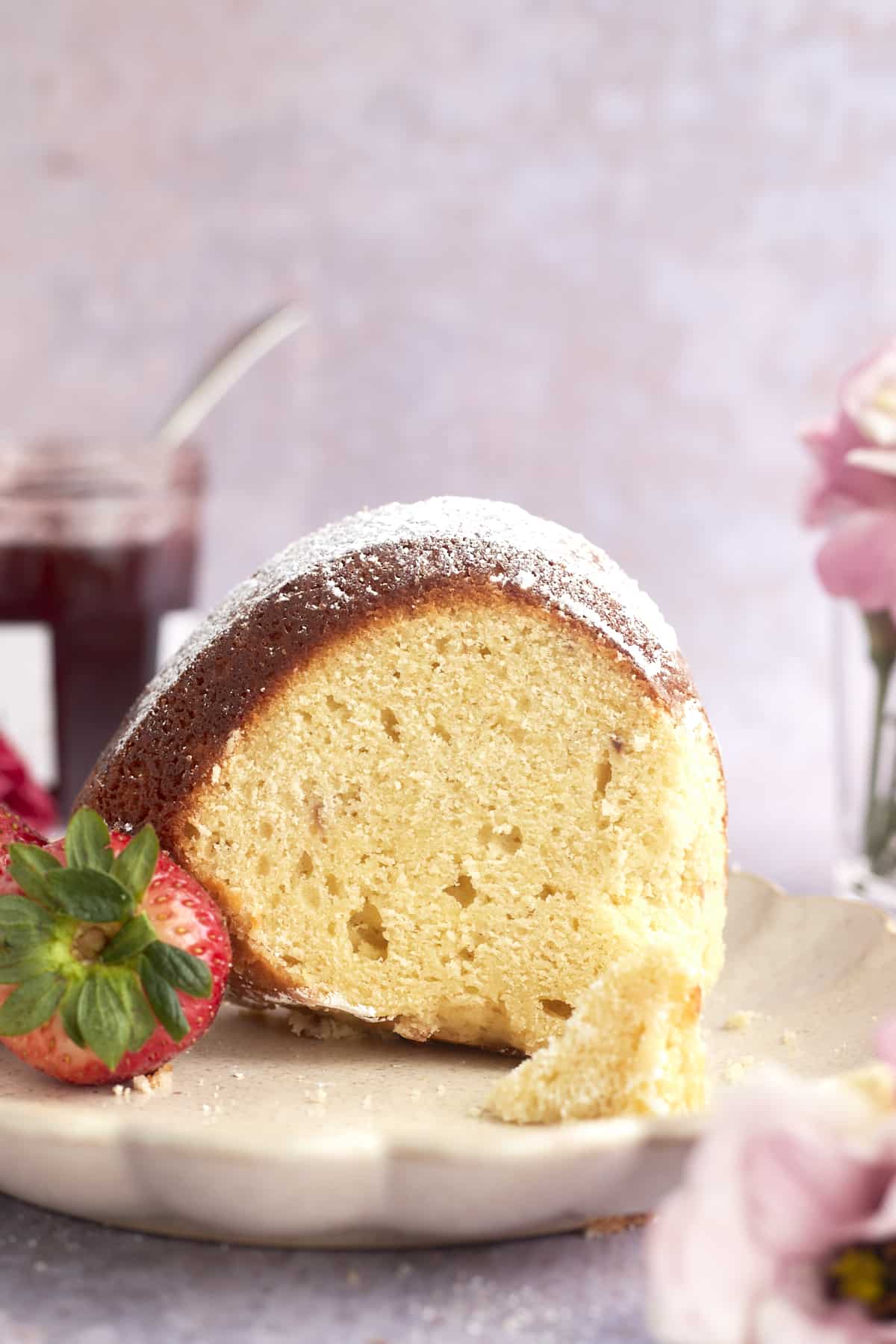 side view of a slice of bundt cake topped with powdered sugar on a plate with whole strawberries