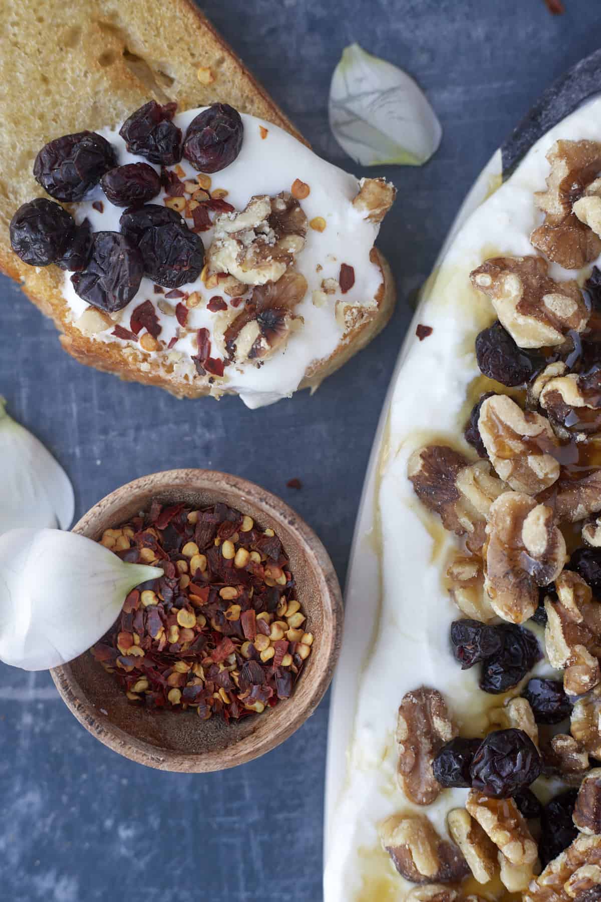 a piece of crostini topped with cranberry and walnut whipped feta with a small bowl of red pepper flakes on the side