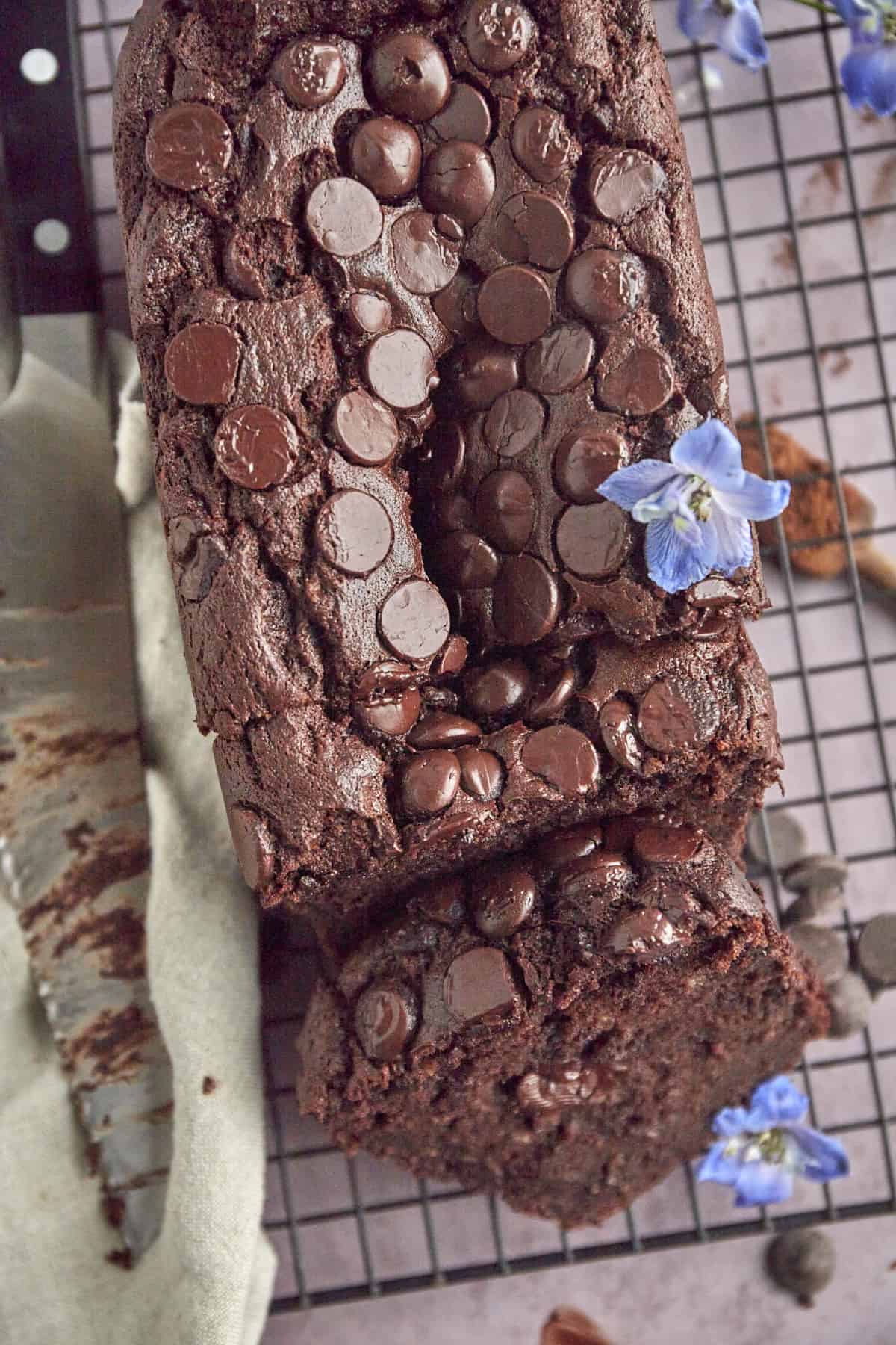 a loaf of double chocolate banana bread on a wire rack with one slice cut