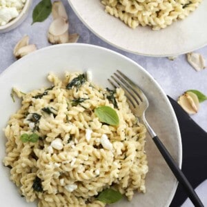 two bowls of spanakopita pasta with spinach topped with fresh herbs