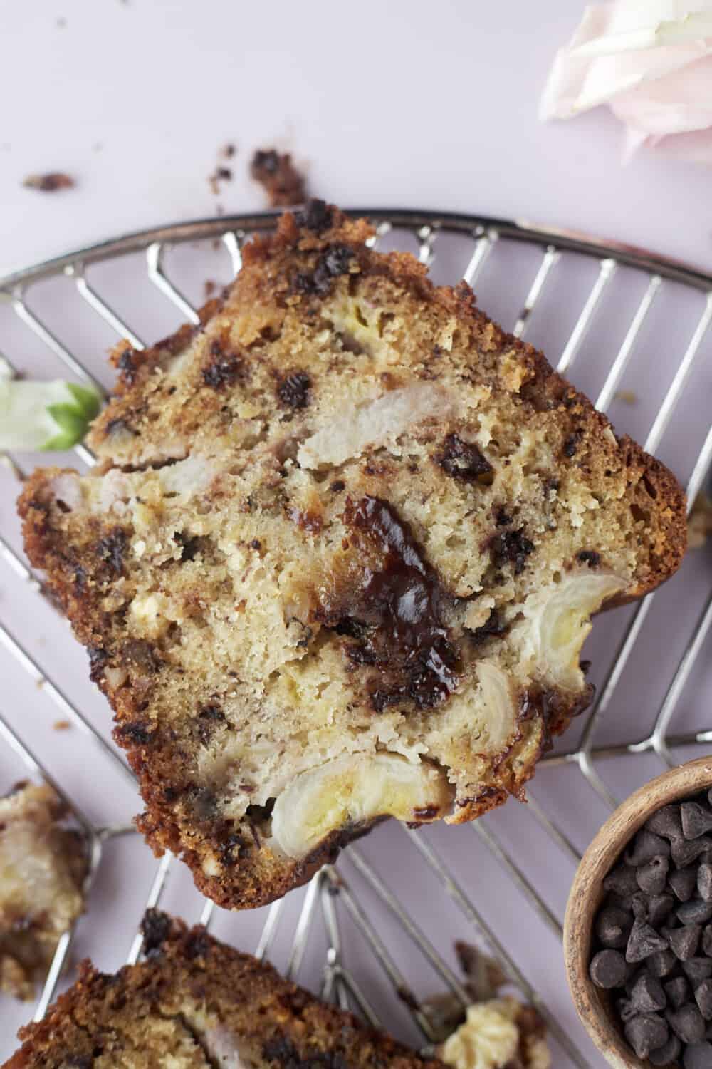 a slice of easy banana bread with semi-sweet and white chocolate chips, walnuts, and banana pieces on a wire rack