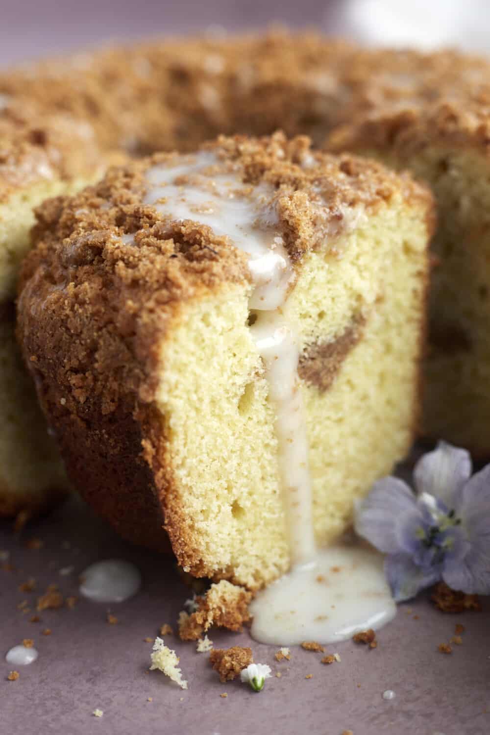 a close up image of a slice of sour cream coffee cake with glaze dripping down