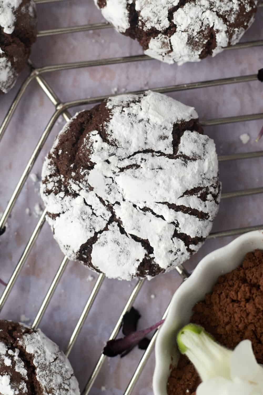 close up image of a powdered sugar coated chocolate crinkle cookie on a wire rack