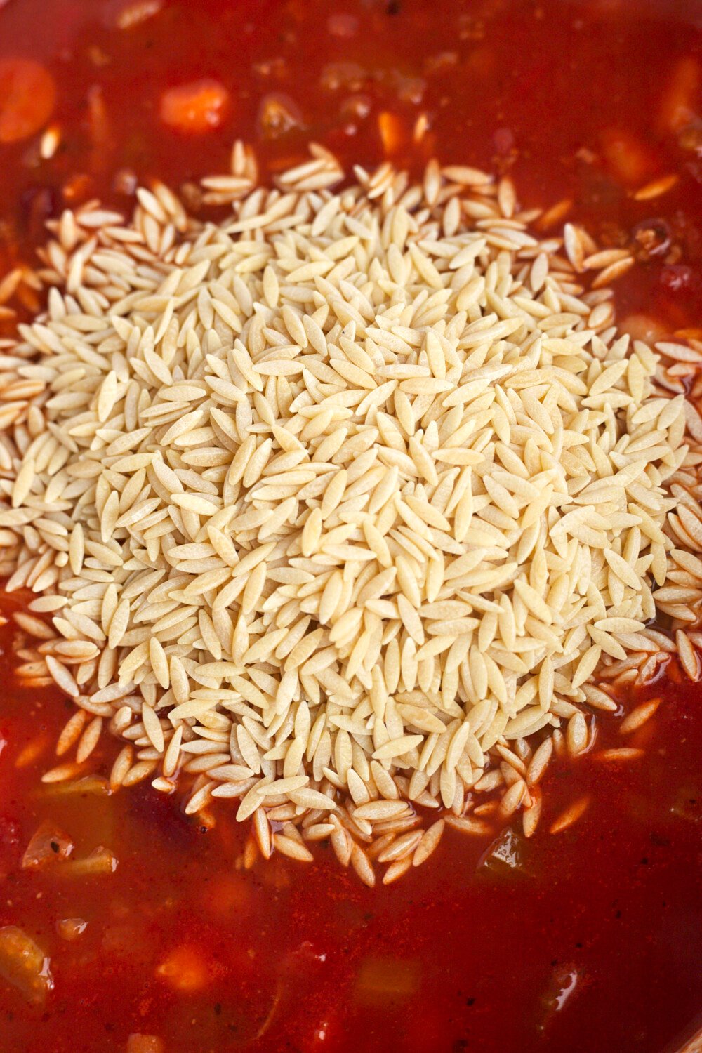 uncooked orzo on top of pasta sauce