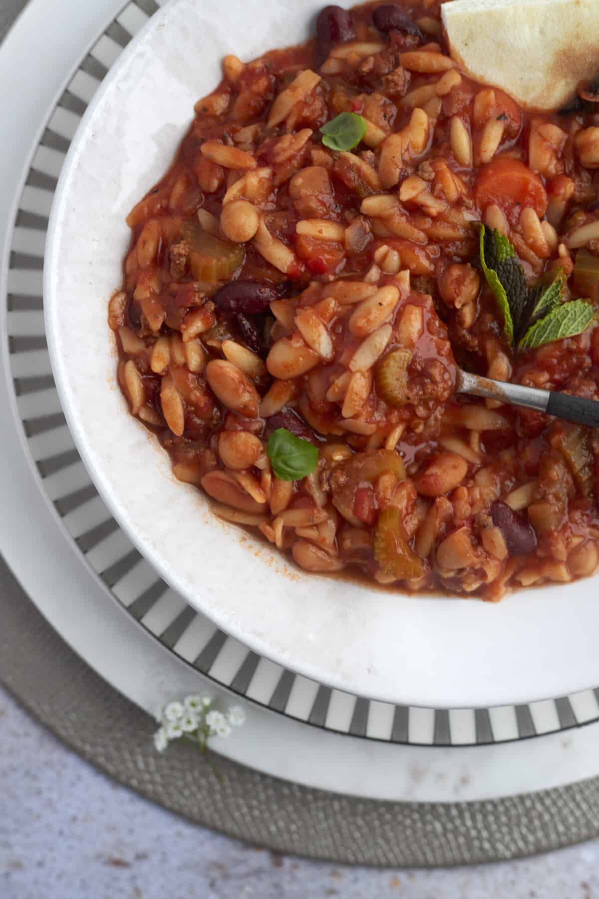 overhead image of a bowl of pasta e fagioli with a spoon dipped in and bread on the side