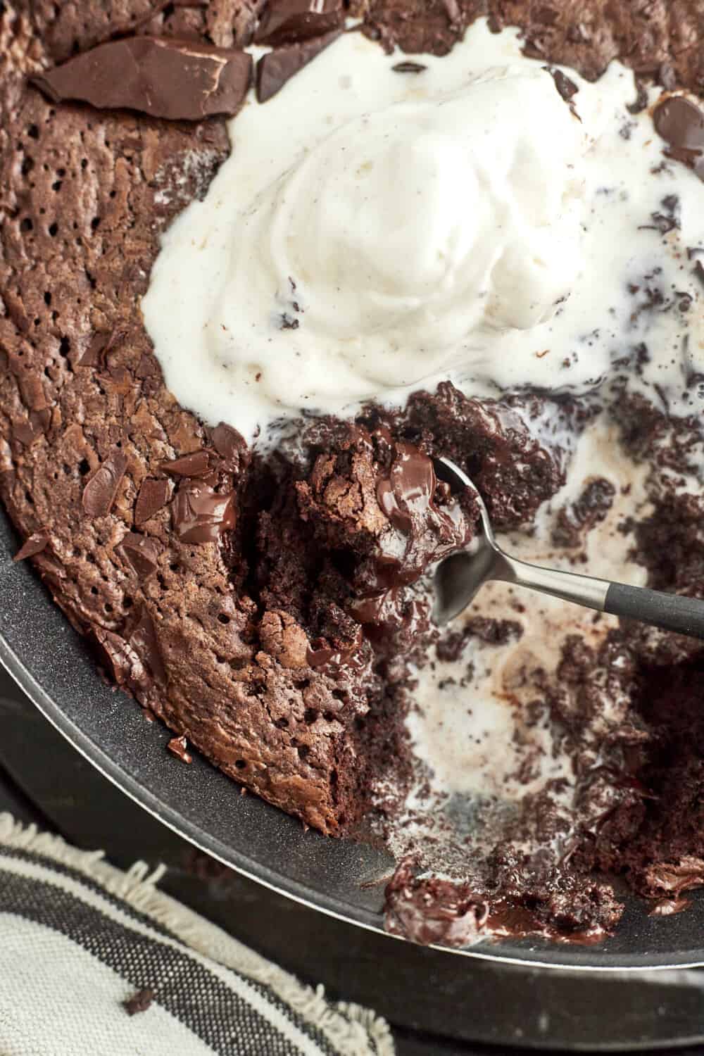 close up image of a spoon digging into a brownie topped with vanilla ice cream