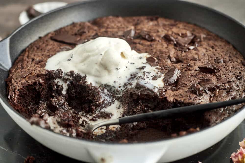 side image of a half-eaten brownie in a skillet topped with melting ice cream