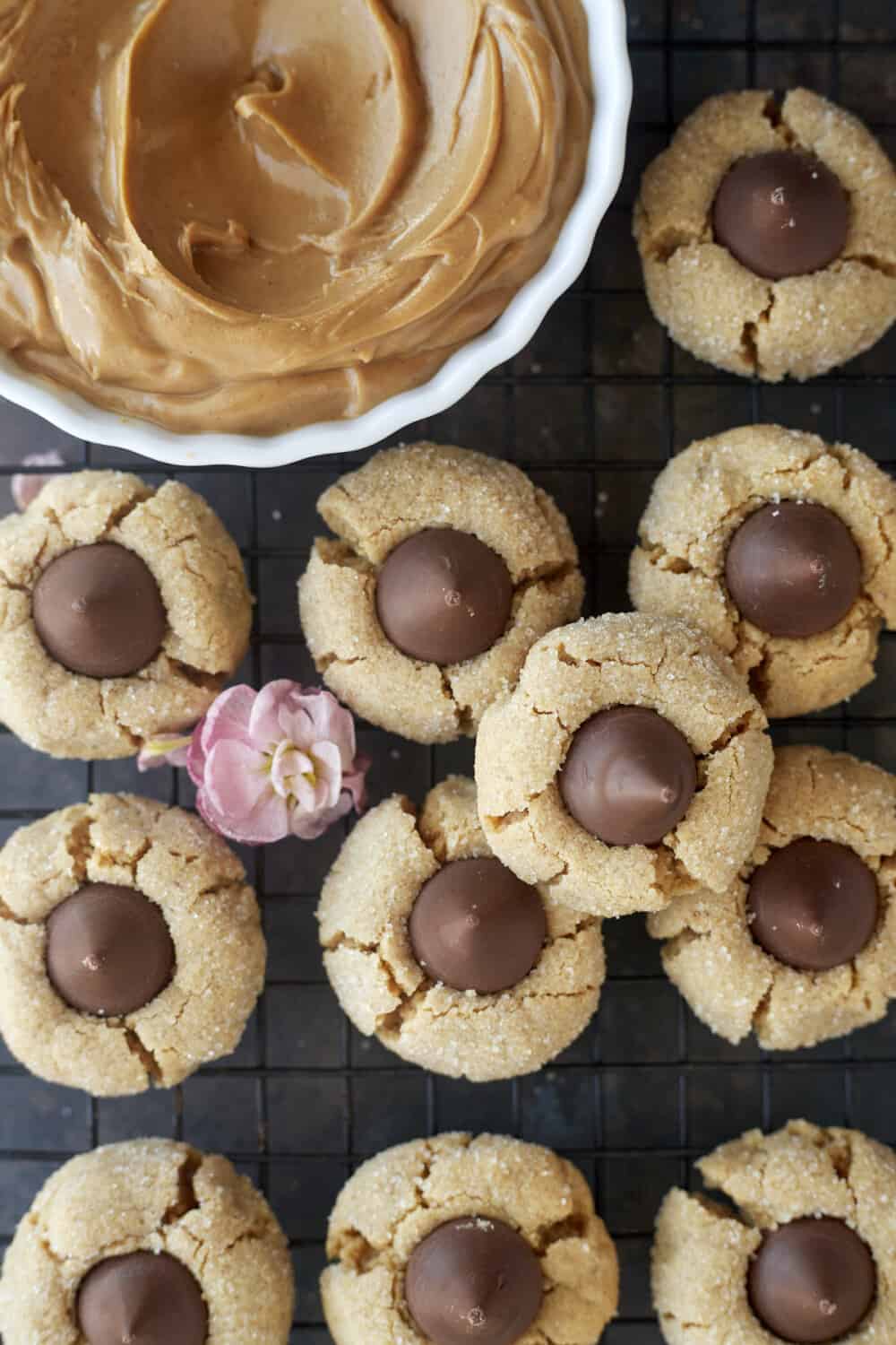 peanut butter blossoms on a cooling rack with a bowl of peanut butter on the side