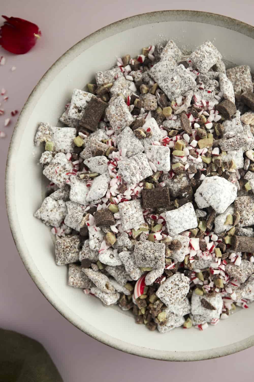 a bowl of Christmas puppy chow with dark chocolate chunks, Andes mints, and peppermint pieces