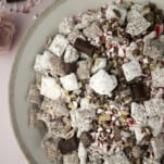 bowl of Christmas puppy chow with chocolate chunks, Andes mints, and peppermint pieces.