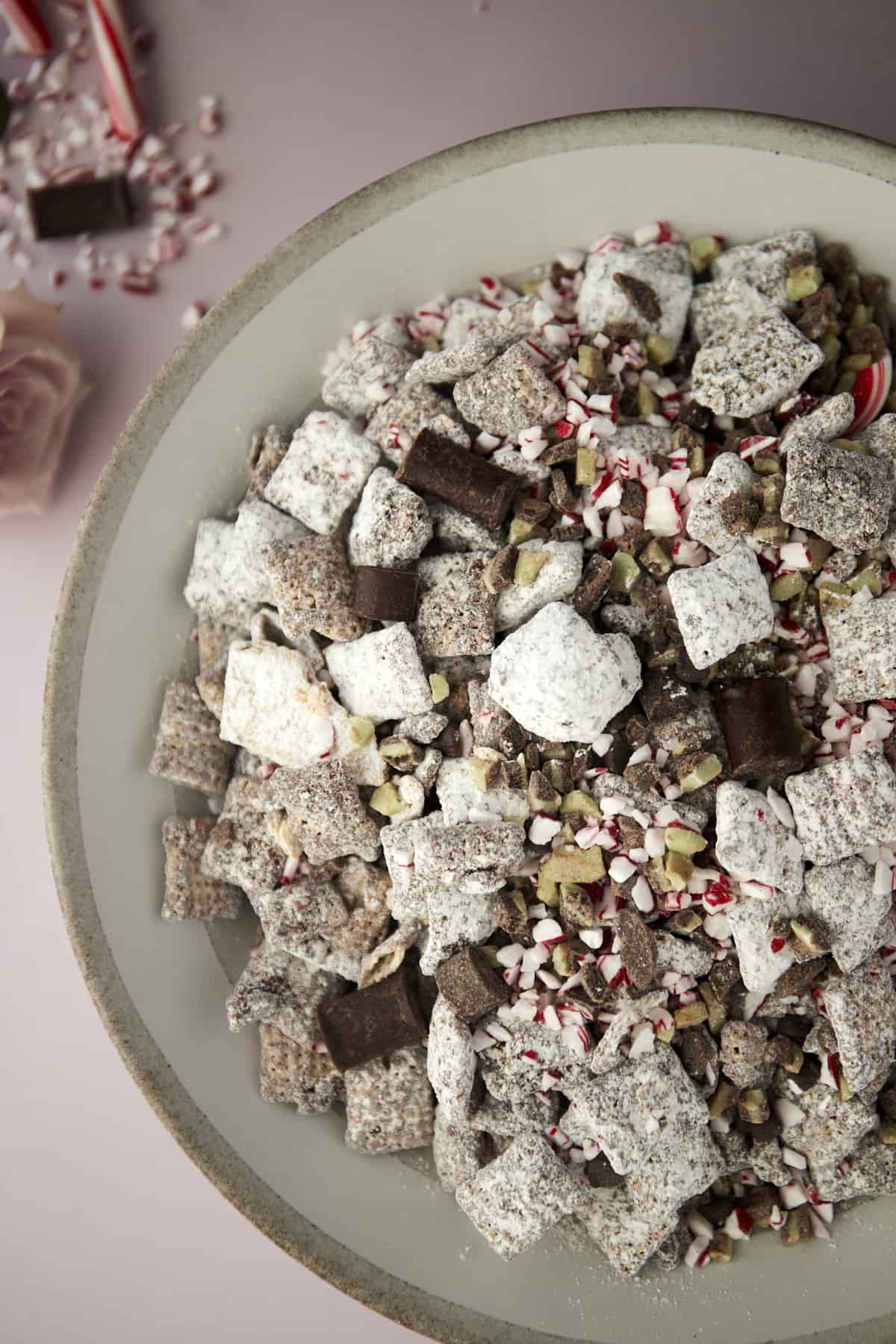 bowl of Christmas puppy chow with chocolate chunks, Andes mints, and peppermint pieces.