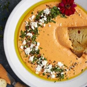 crostini dipped into a bowl of roasted red pepper whipped feta dip