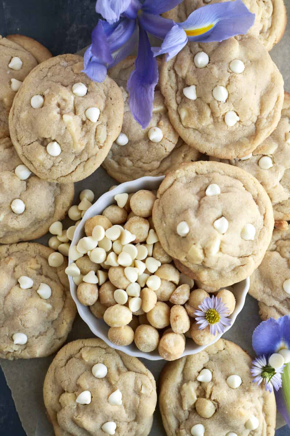 a batch of white chocolate macadamia nut cookies with a bowl of white chocolate and macadamia nuts in the center