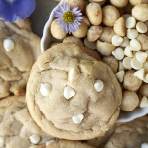 close up image of a white chocolate macadamia nut cookie on top of a bowl full of macadamia nuts and white chocolate chips