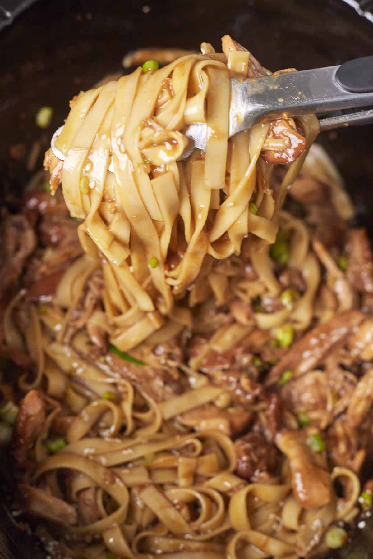 two tongs holding lo mein noodles with chicken and a honey garlic sauce