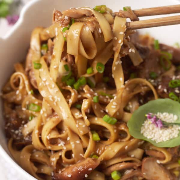 a bite of honey garlic chicken lo mein noodles being lifted with chopsticks