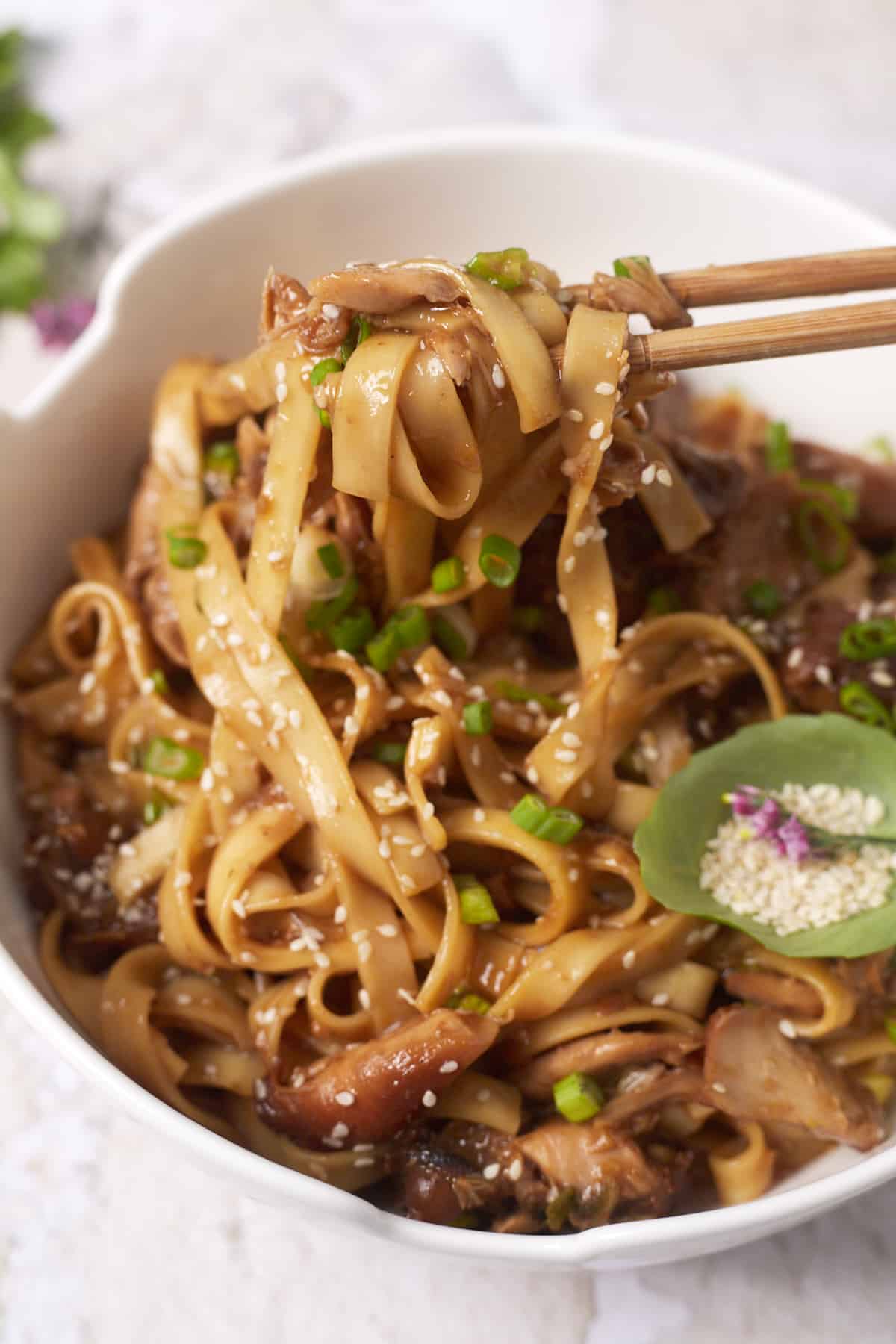 Chopsticks holding a bite of lo mein noodles and chicken in a honey garlic sauce