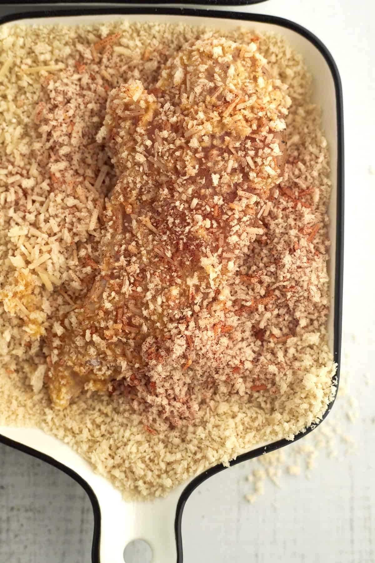 raw chicken being coated with breadcrumbs