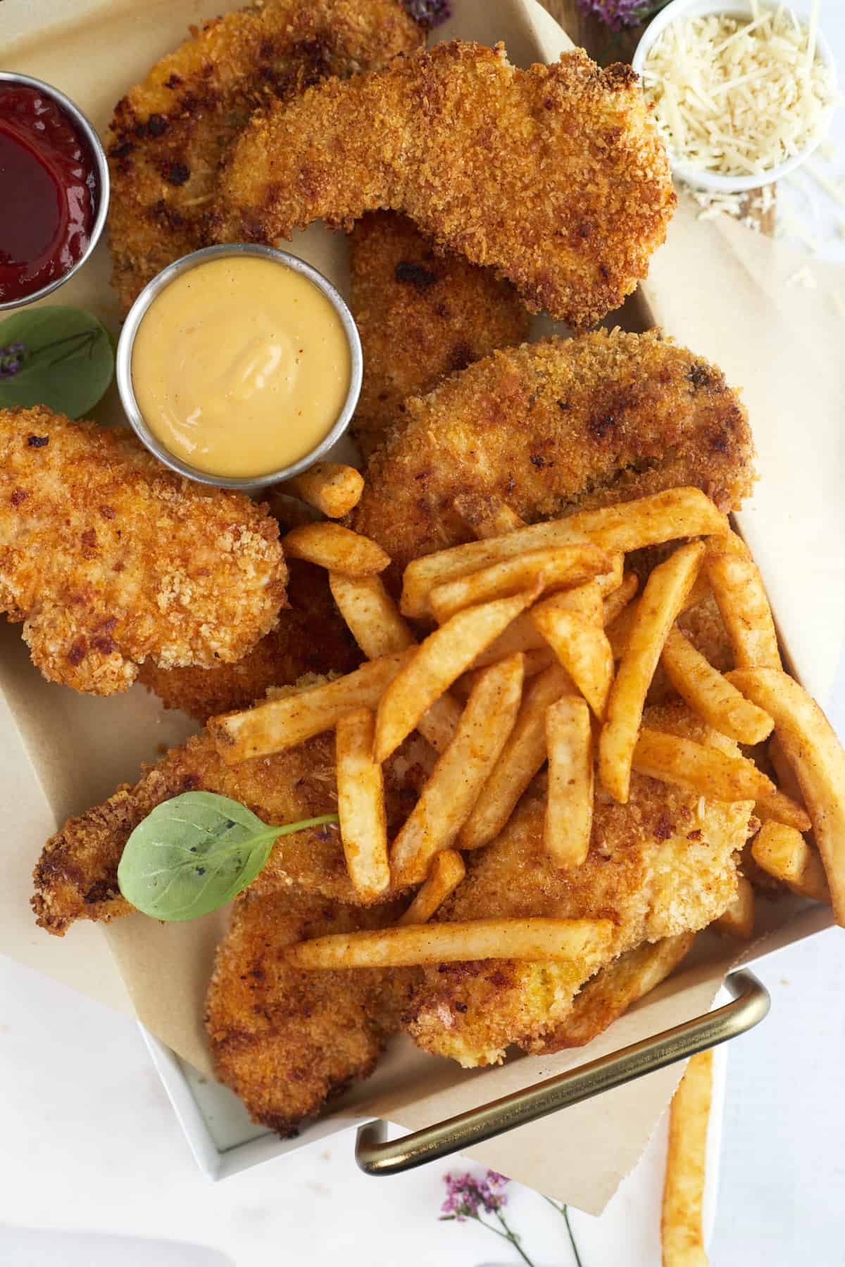 parmesan chicken tenders on a baking sheet with fries and honey mustard sauce