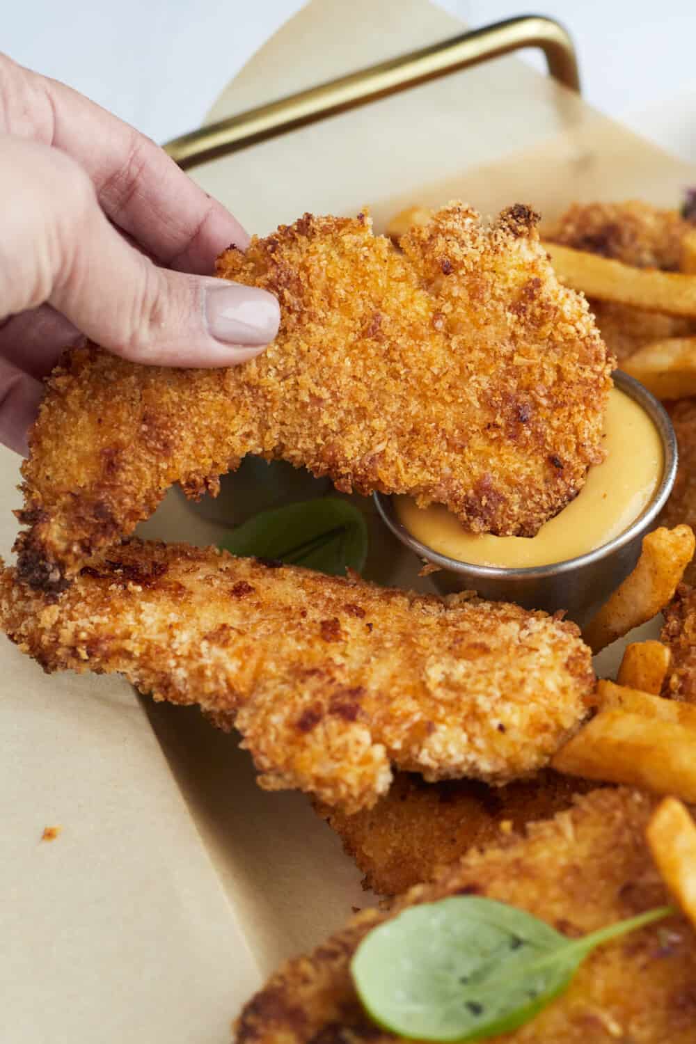 a breaded chicken tender being dipped into honey mustard sauce