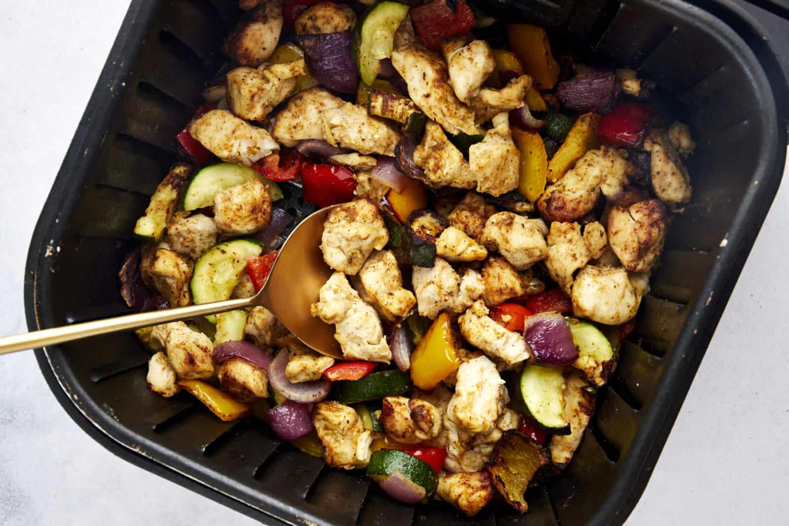 a spoon scooping up air fryer chicken breast and vegetables from an air fryer