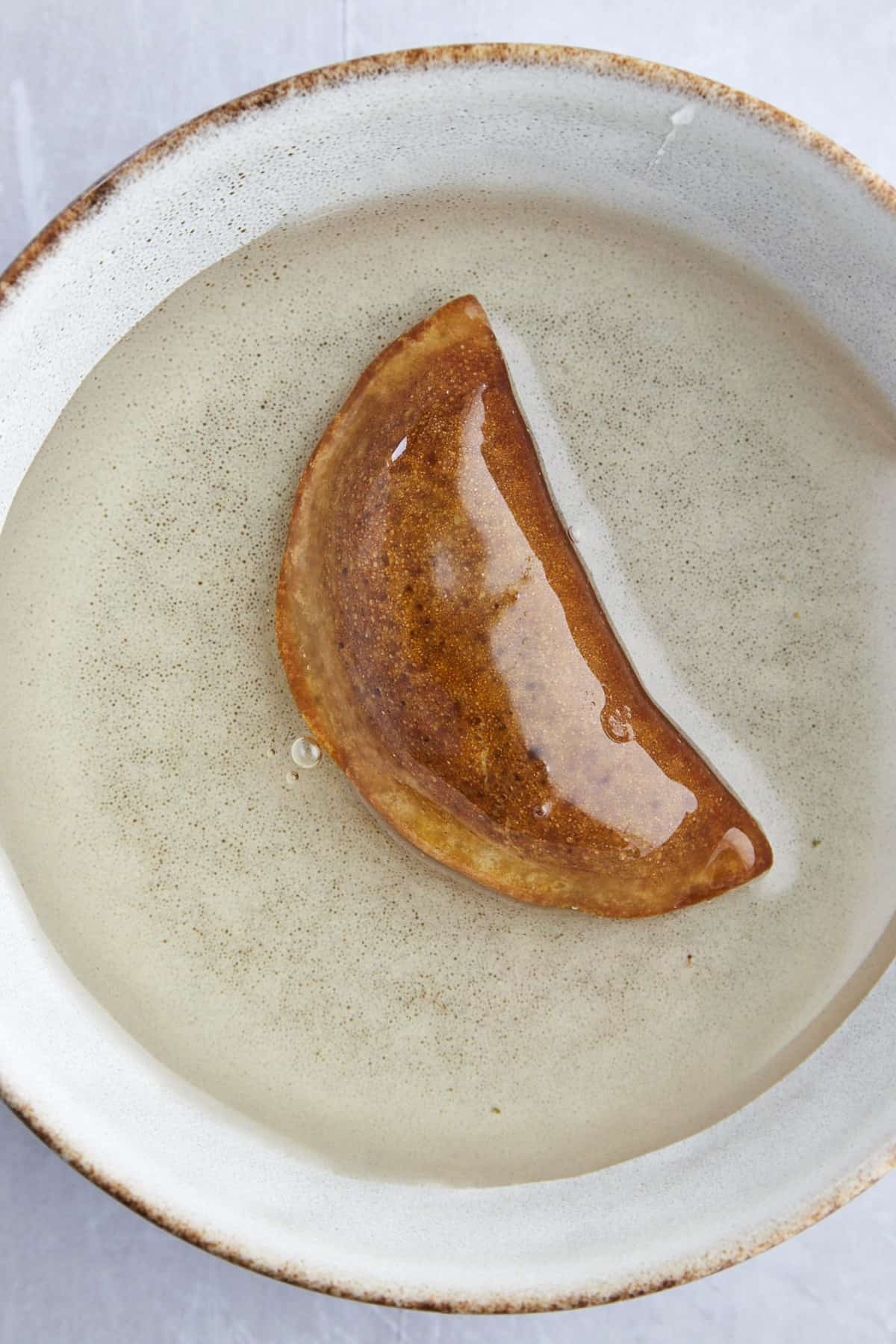 an atayef piece in a bowl of simple sugar