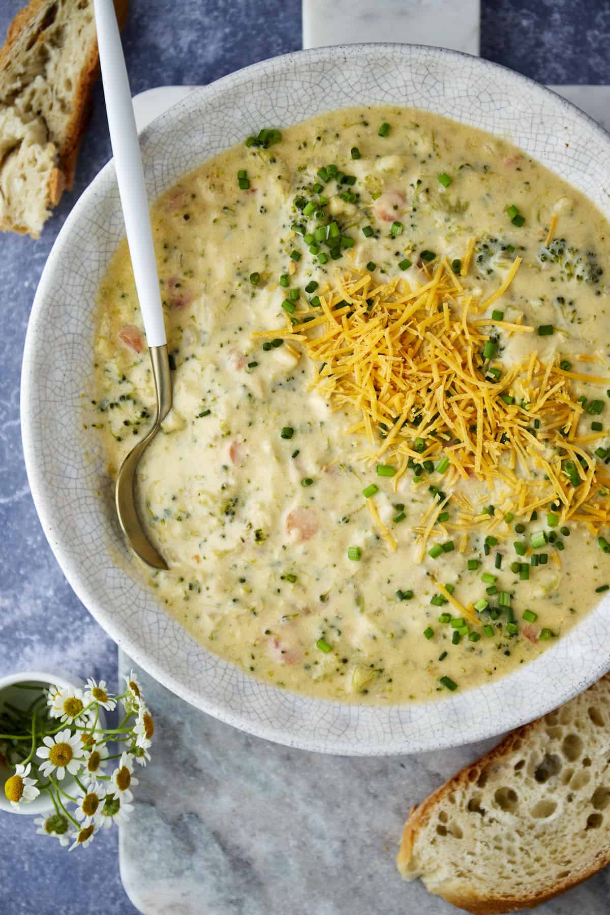 A bowl of broccoli and cheese soup topped with shredded cheddar with a spoon. 