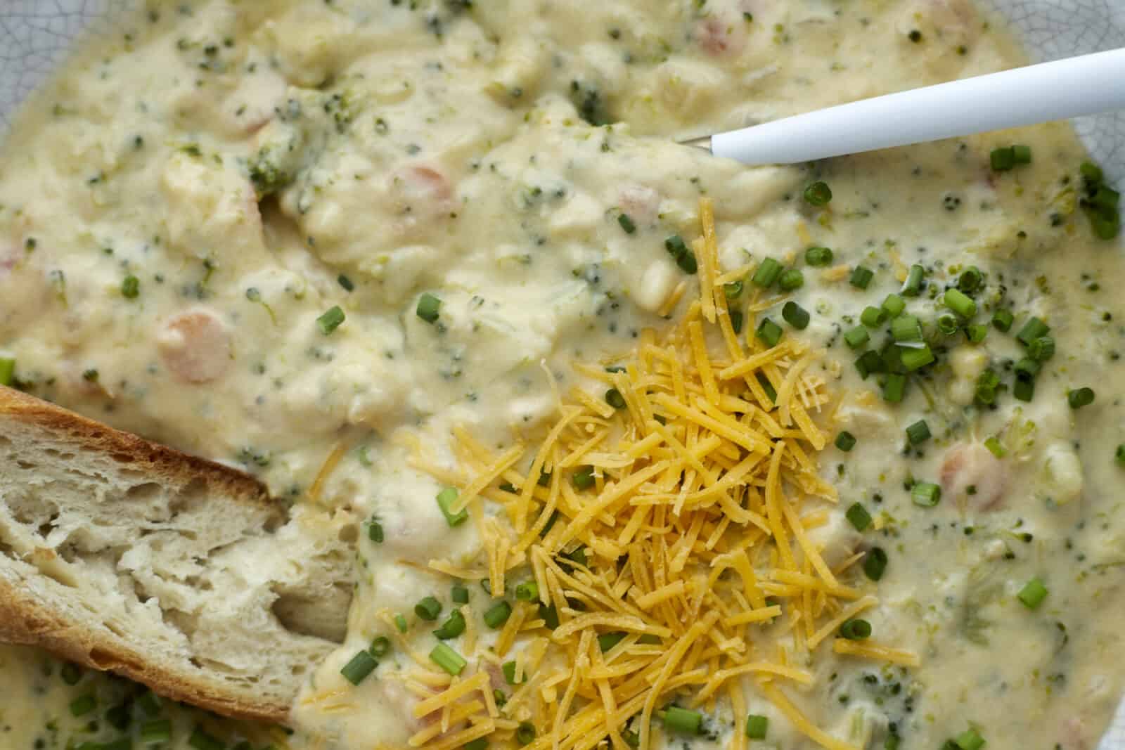 a piece of bread dipped into a bowl of broccoli and cheese soup.