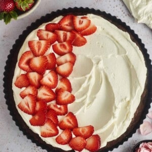 overhead image of a chocolate brownie pizza tart topped with cream cheese frosting and sliced strawberries