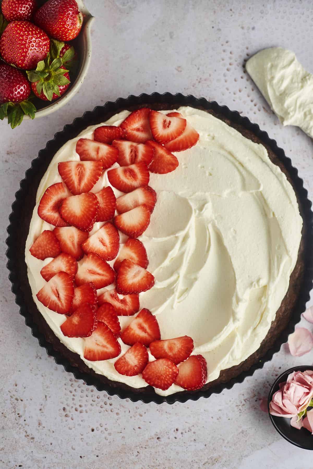 a chocolate brownie pizza tart topped with whipped cream frosting and sliced strawberries