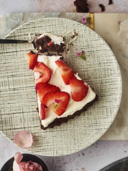 a slice of a brownie pizza tart on a plate with a forkful of the dessert on the side