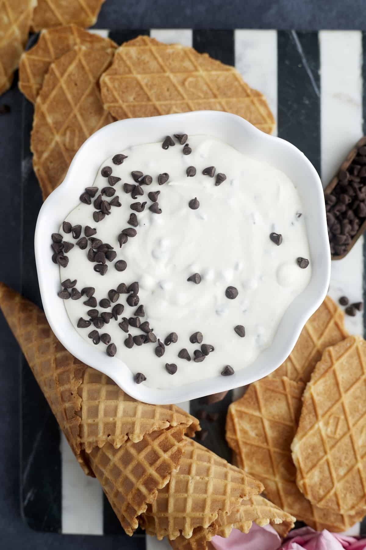 a bowl of cannoli dip topped with chocolate chips surrounded by waffle cones