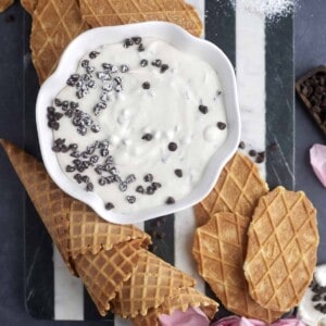 a bowl of cannoli dip topped with chocolate chips with waffle cones around