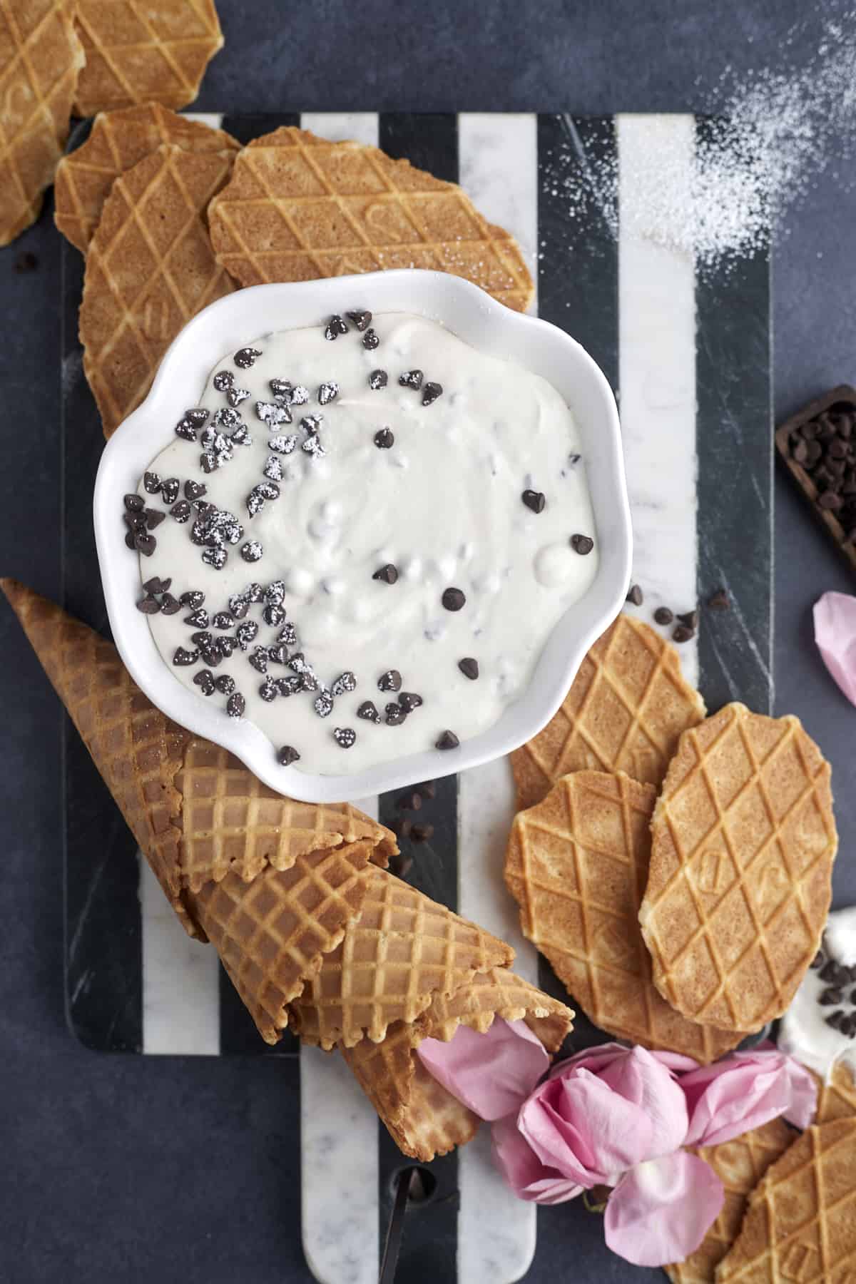 a bowl of cannoli dip topped with chocolate chips with waffle cones around