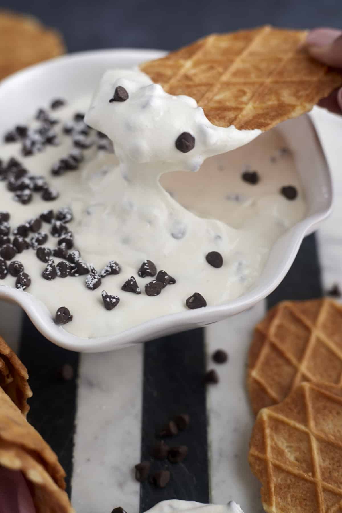 a piece of waffle cone being dipped into cannoli dip