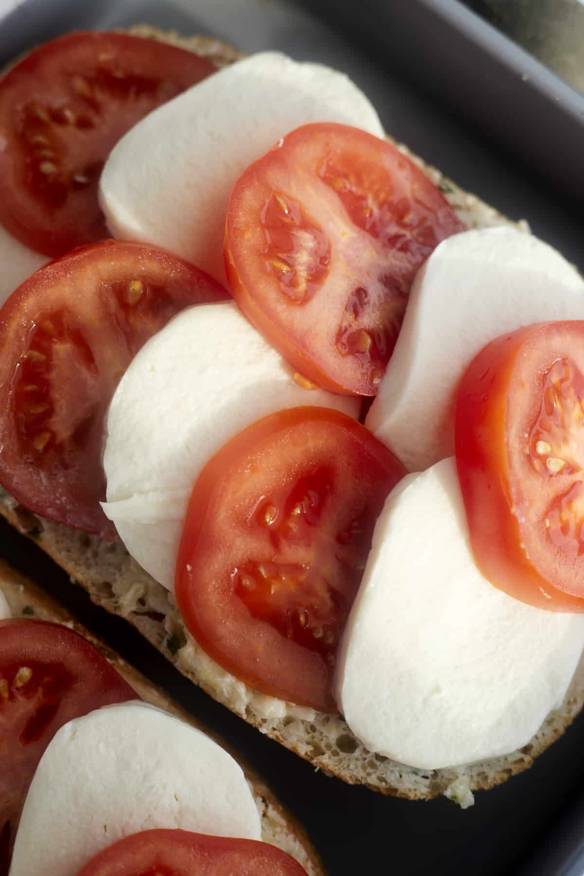 unbaked bread topped with garlic butter, tomato, and mozzarella 