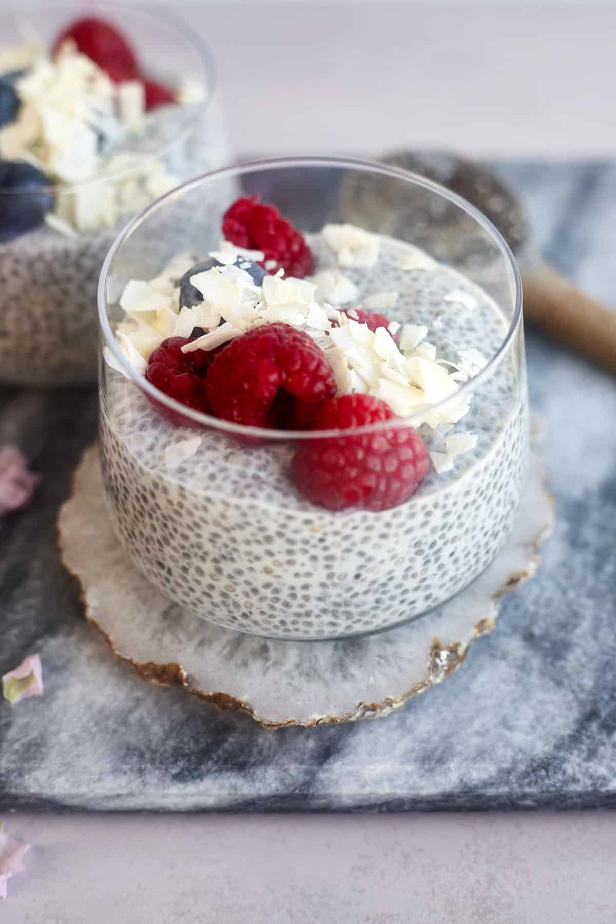 a jar of coconut chia pudding topped with raspberries, blueberries, and coconut flakes