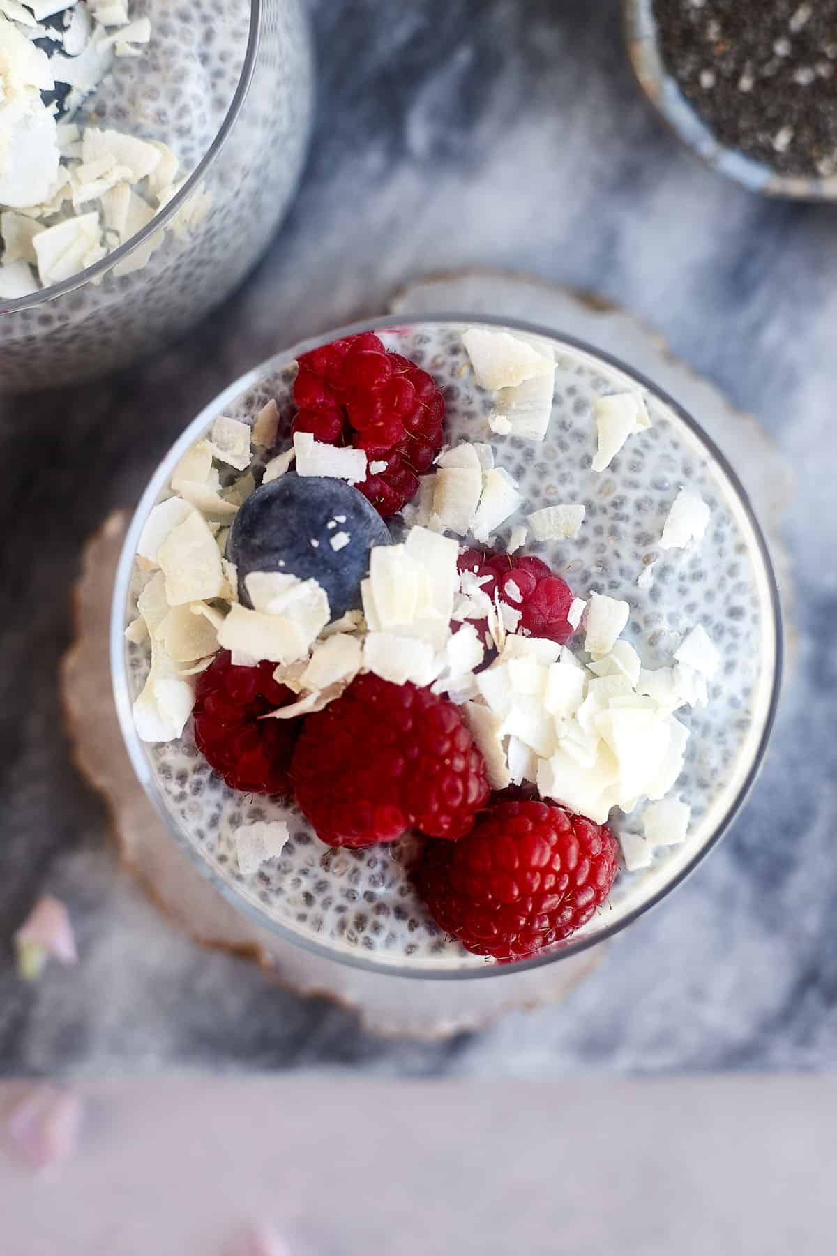 overhead image of coconut chia pudding topped with fresh raspberries, blueberries, and coconut flakes